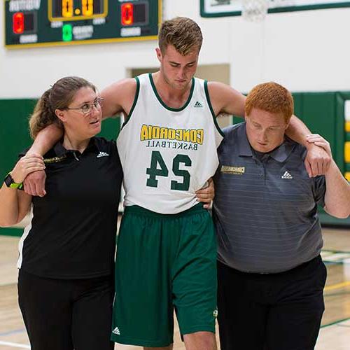 Athletic training students helping an athlete off the court.